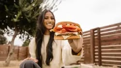 A woman holding a Sourdough Jack Burger in front of the camera while smiling 250 WebP-1